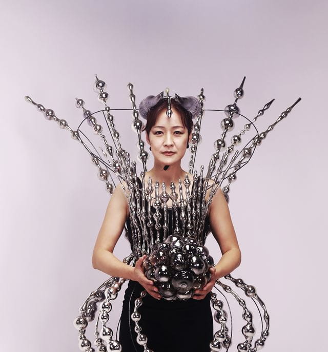 Instructor Jin Won Han wears an outfit made of glass while holding a glass ball.