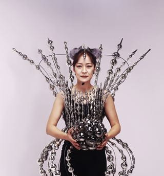 Instructor Jin Won Han wears an outfit made of glass while holding a glass ball.