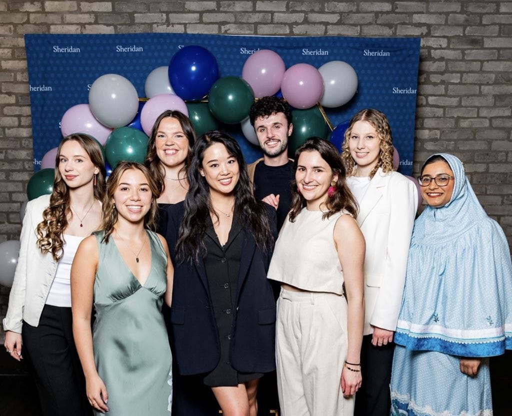 Francesca Mak stands with fellow Interior Design students in front of a Sheridan backdrop and balloons