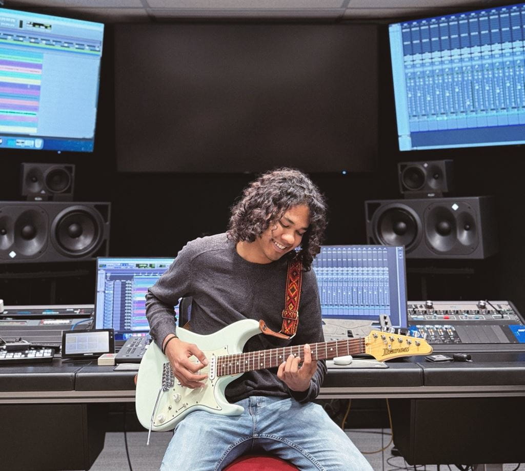 Music Scoring for Screen and Stage student Ricardo Gomes practices his electric guitar while sitting inside one of Sheridan's sound studios
