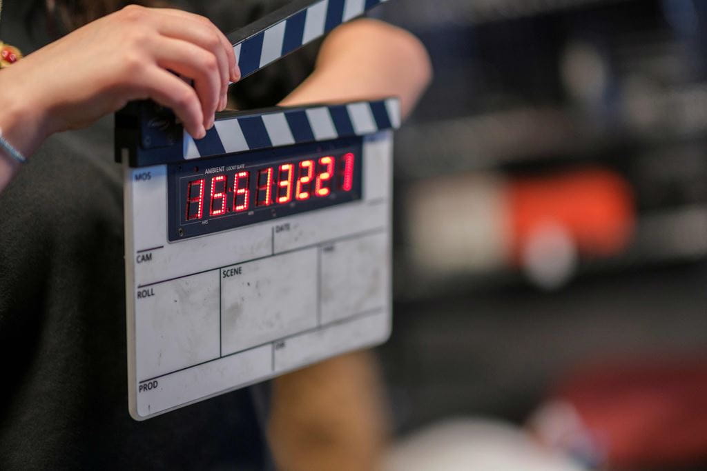 A hand holds a clapperboard with red numbers.