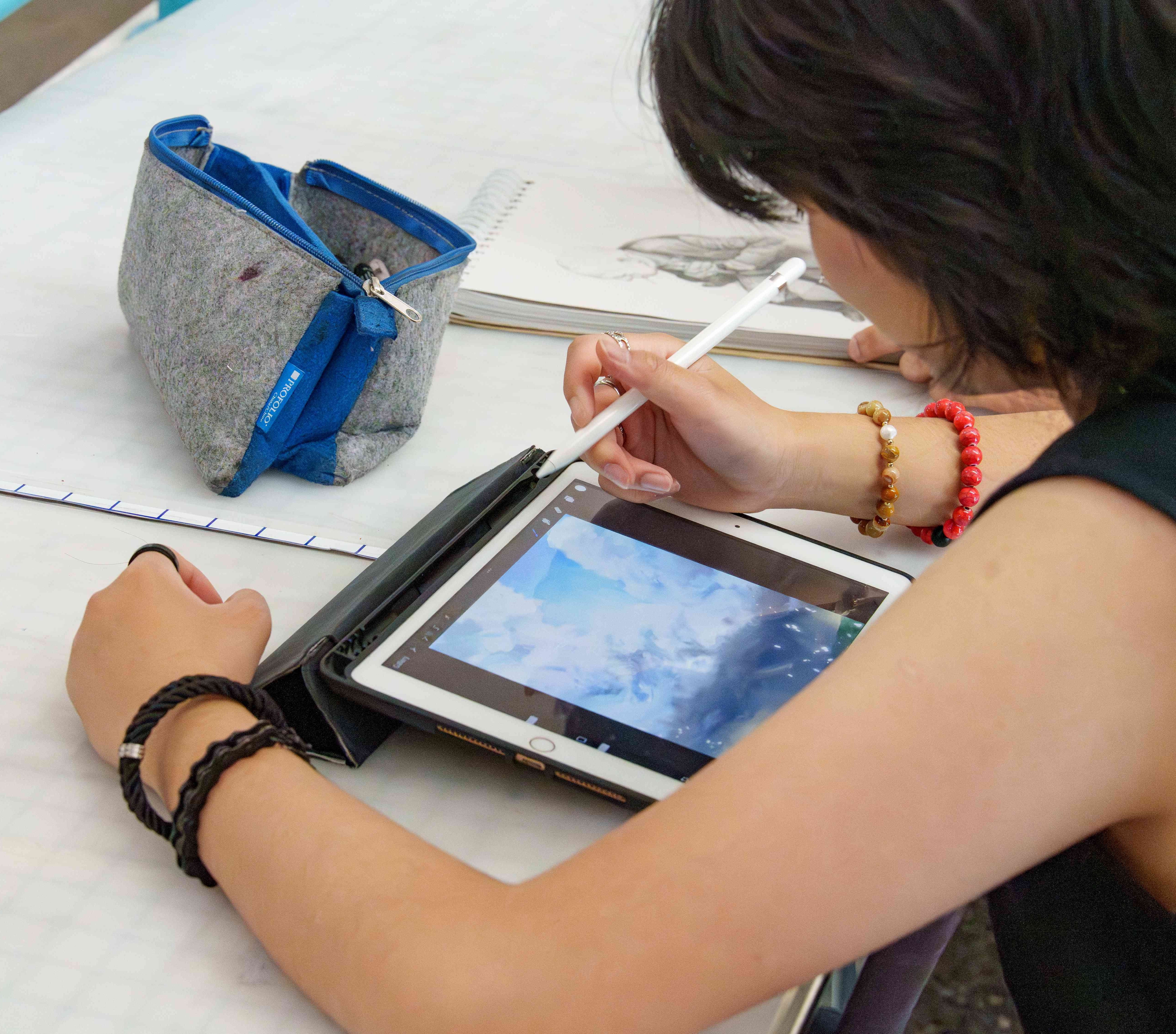 A woman draws on a tablet with a stylus.