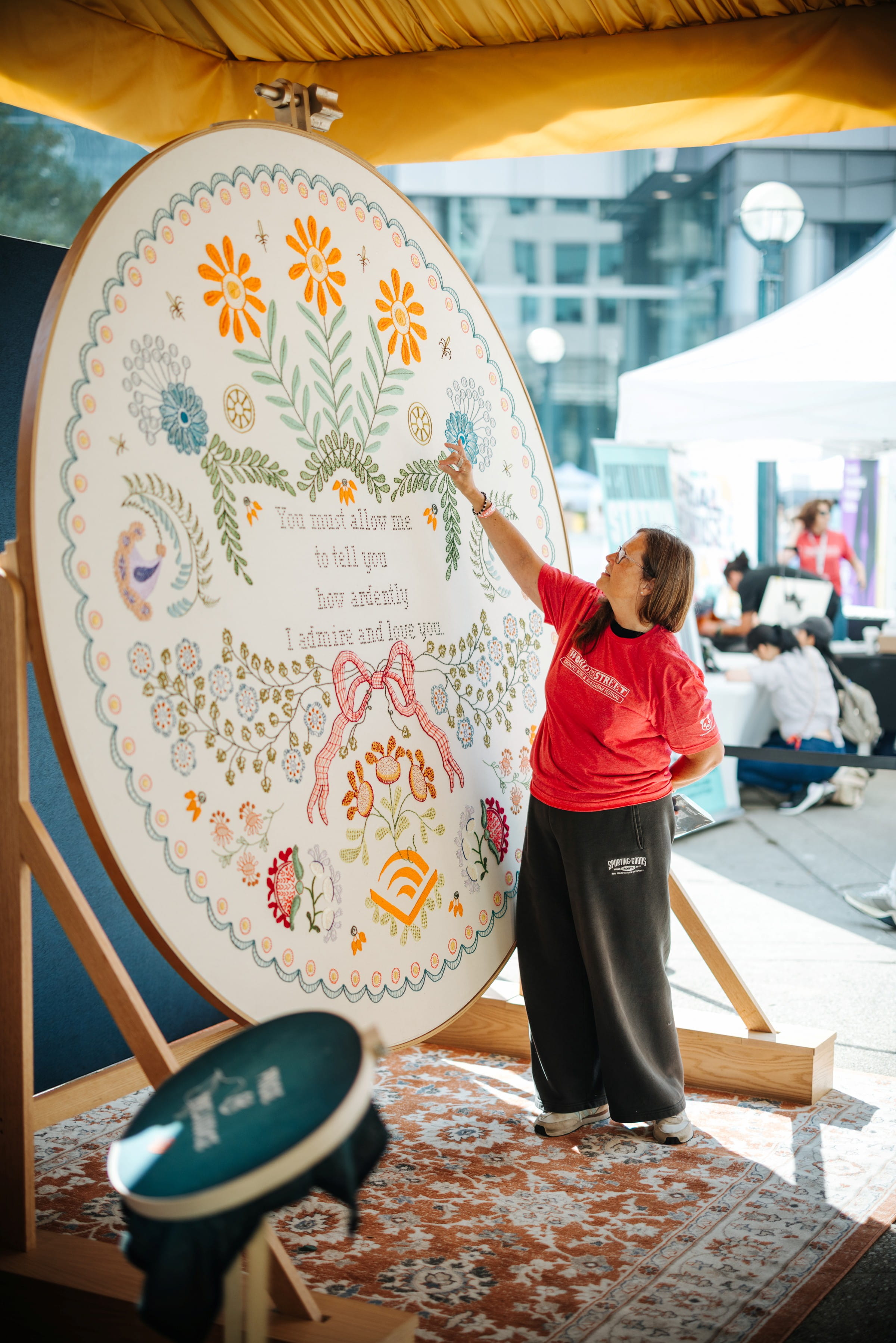 An artist stands next to a large, colourful embroidery mural.