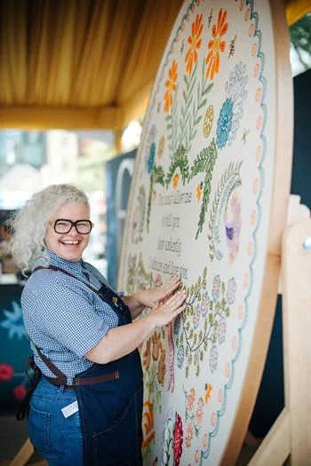 Artist Kate Jackson stands next to a large embroidery mural that she is working on.