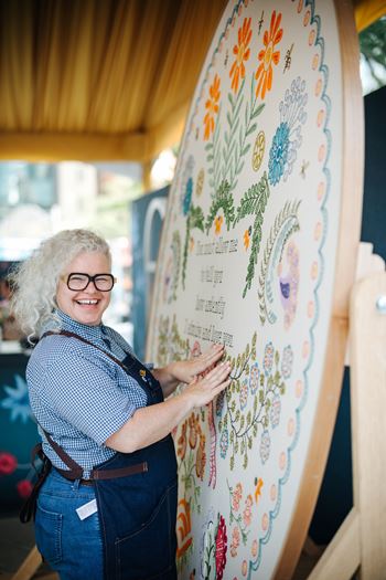Artist Kate Jackson stands next to a large embroidery mural that she is working on.