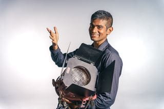 Photography student Tanishq Arun poses for a photo while holding old photography equipment