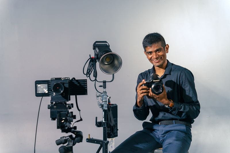 Photography student Tanishq Arun is surrounded by film equipment while holding a camera