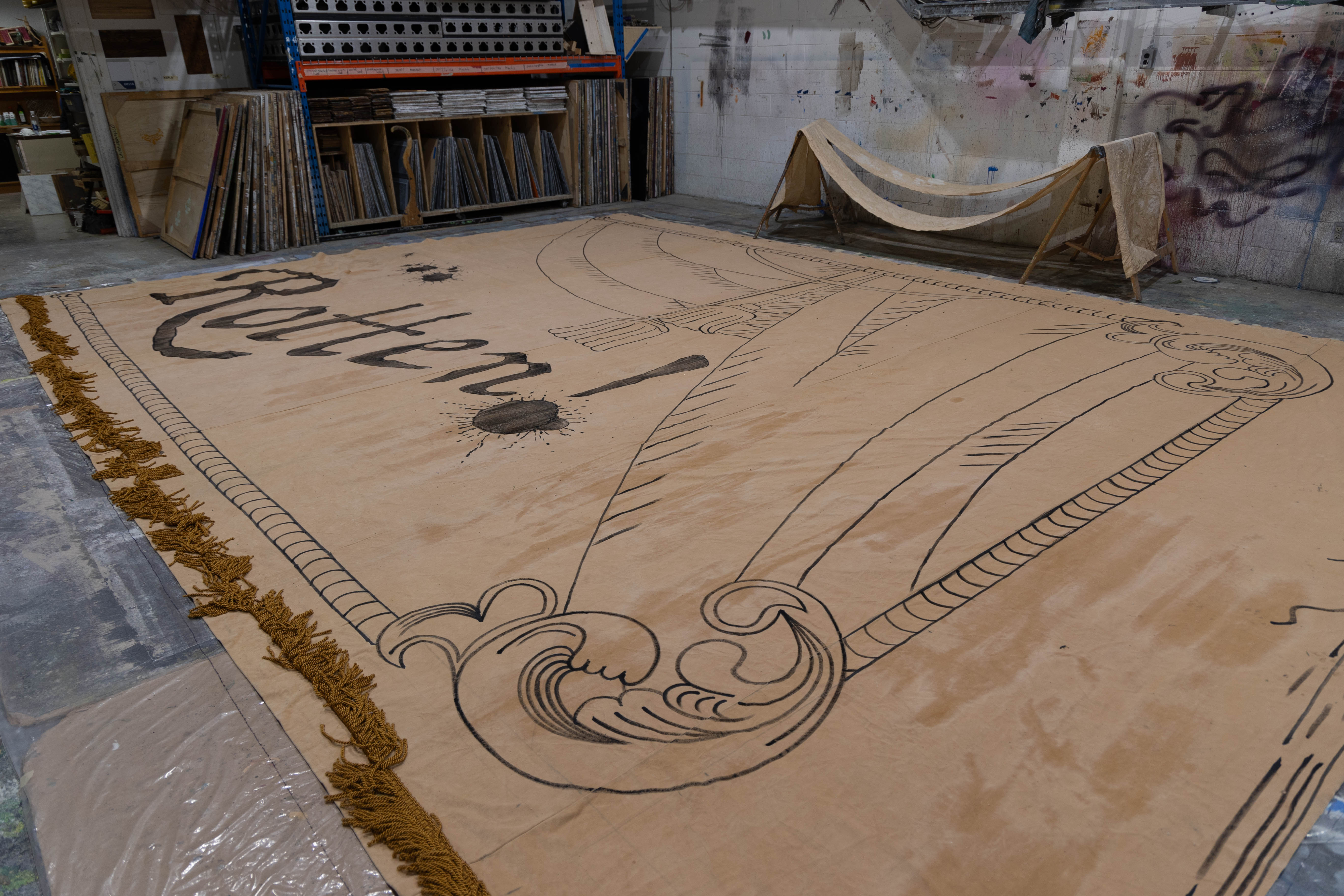 A large beige banner with the word Rotten painted on it sits on the floor of the painting studio.