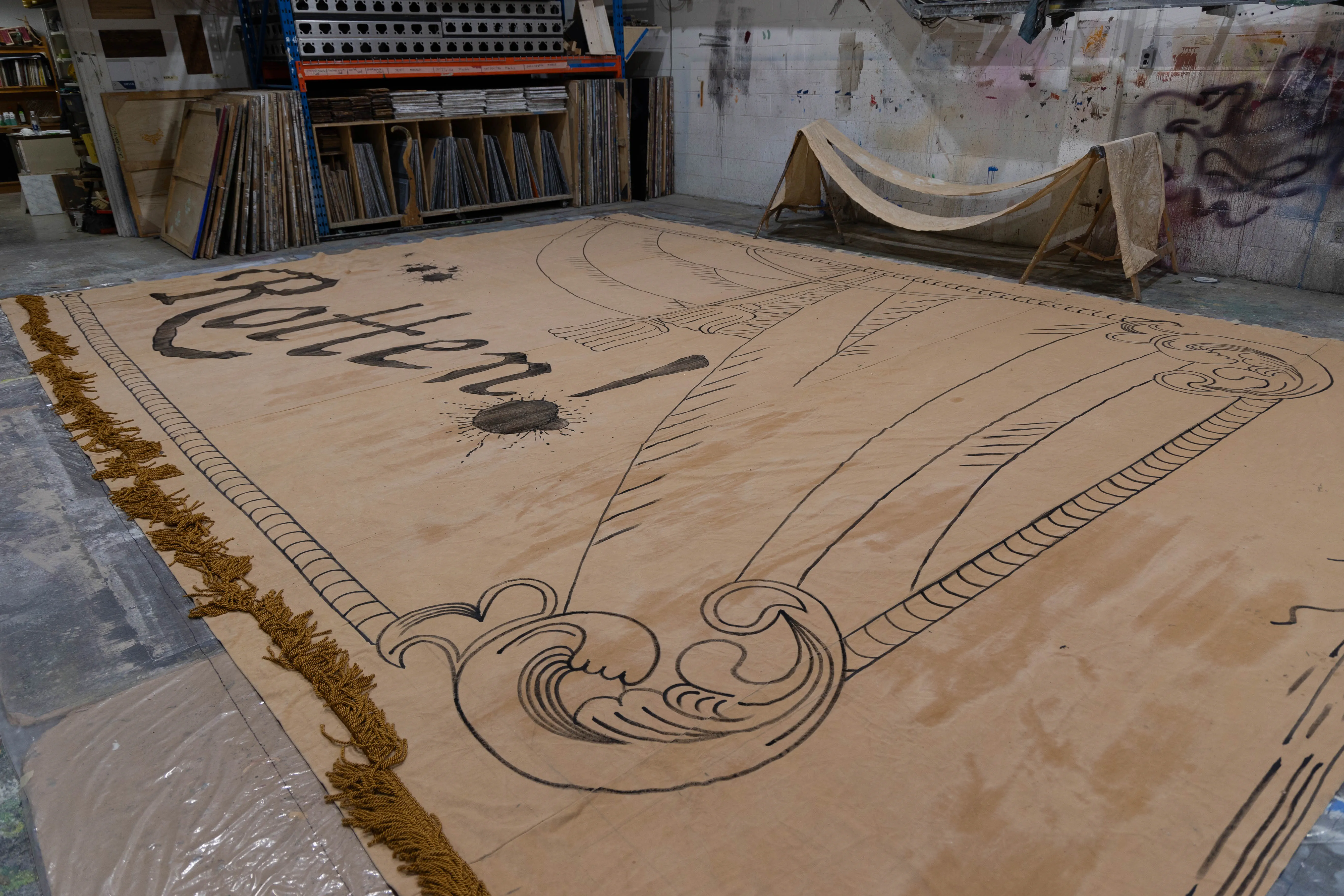 A large beige banner with the word Rotten painted on it sits on the floor of the painting studio.