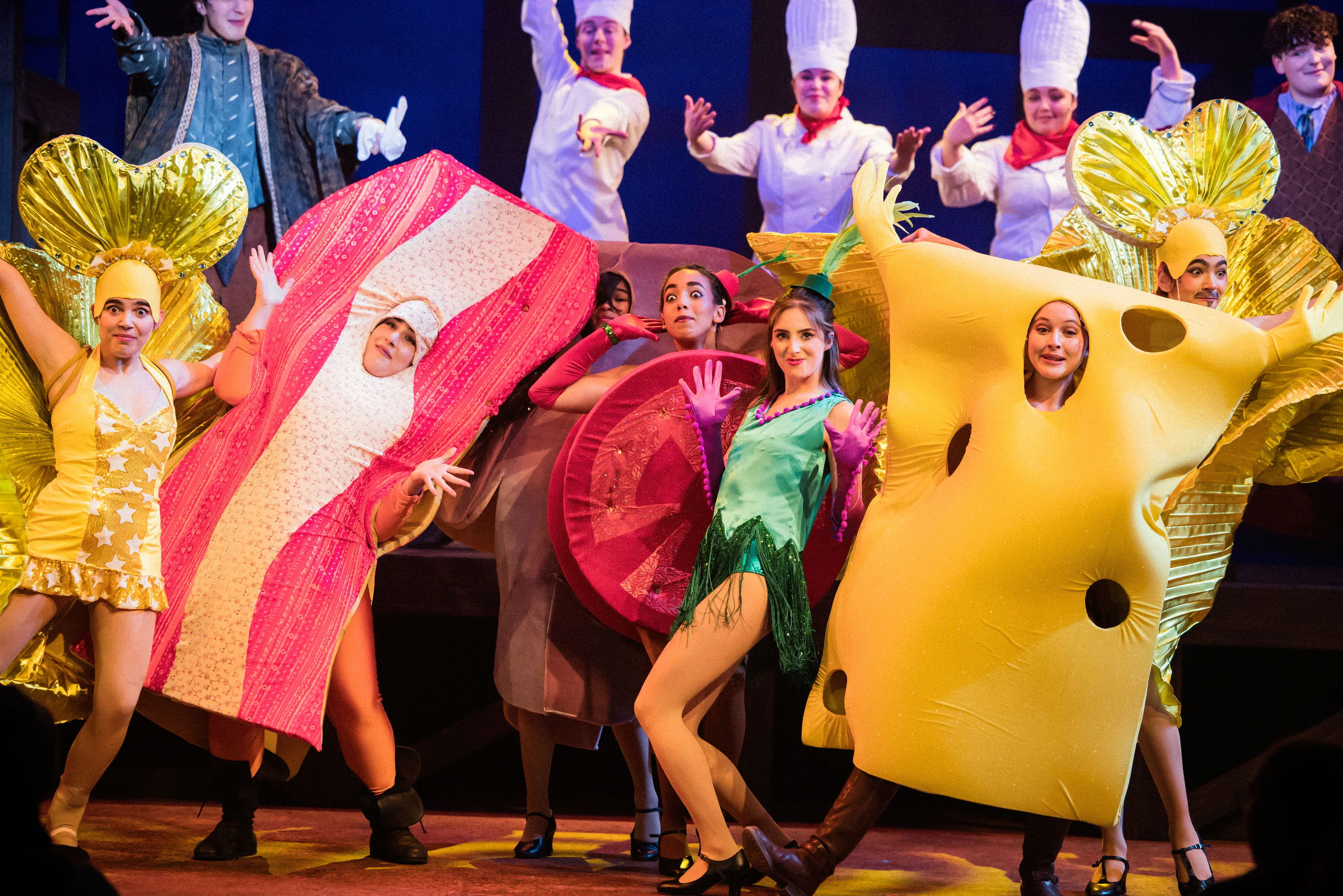 Actors dance on stage wearing colourful costumes such as bacon, tomato and cheese.