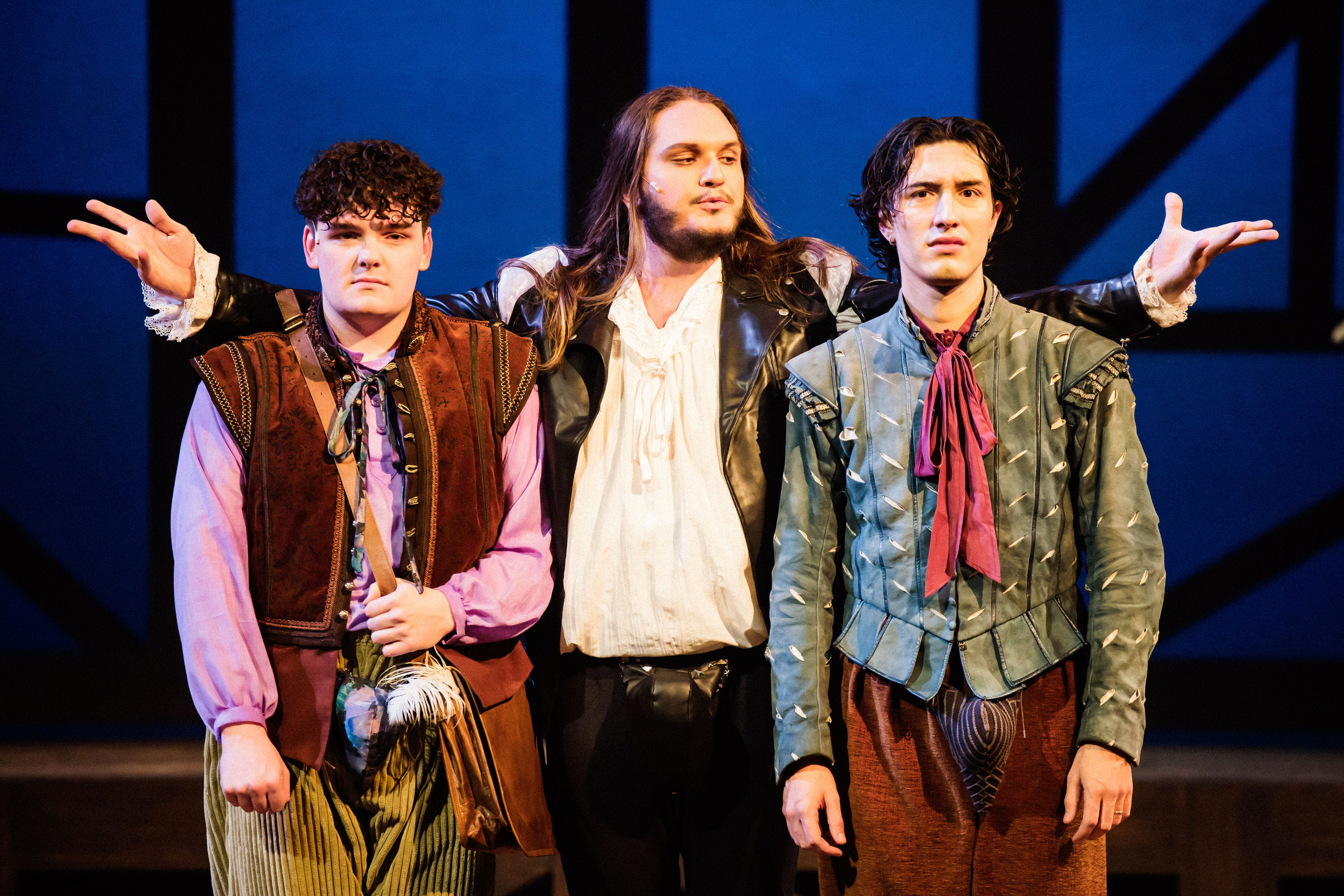 Three male actors face the audience. One plays the role of William Shakespeare and stands between the other actors.