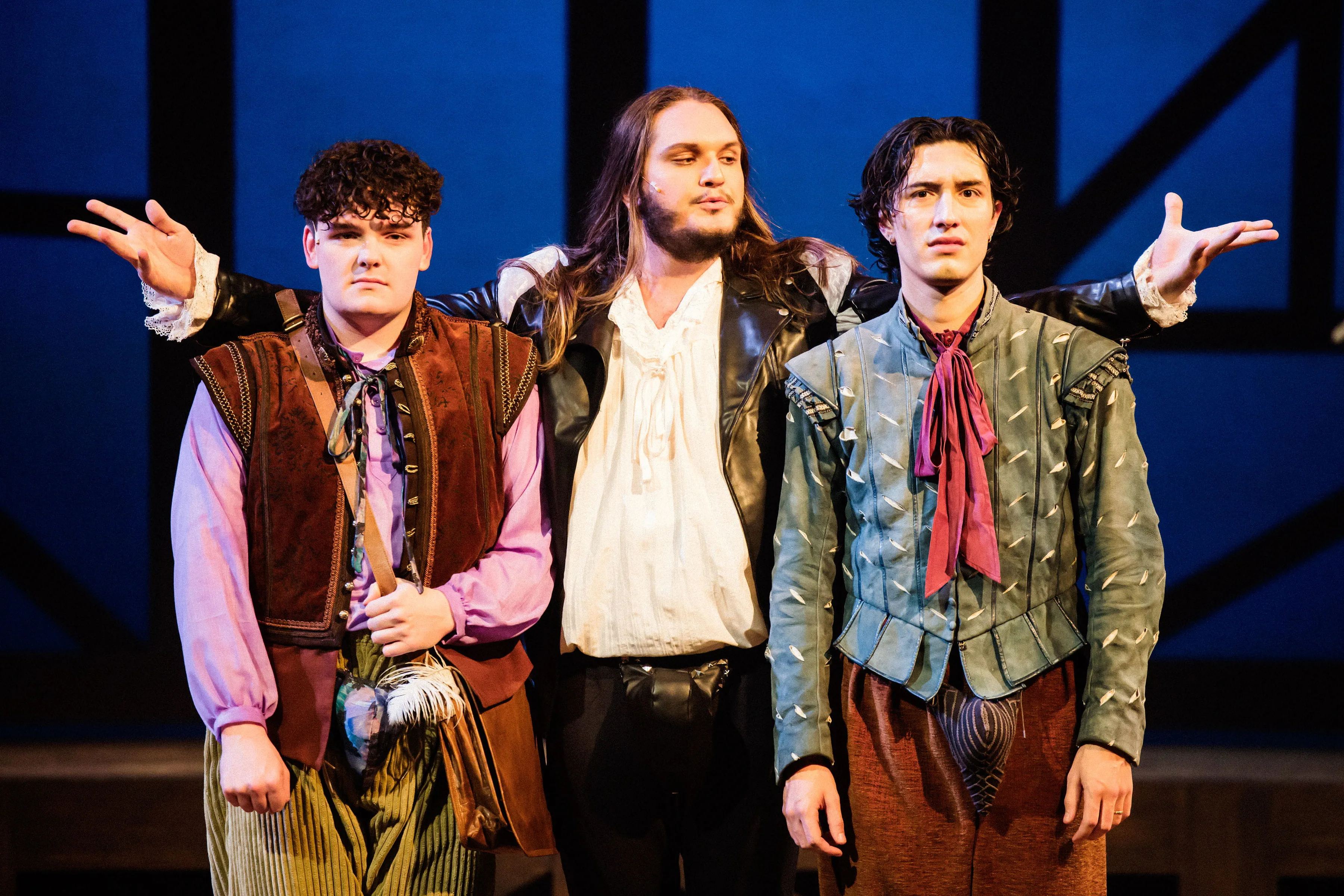 Three male actors face the audience. One plays the role of William Shakespeare and stands between the other actors.