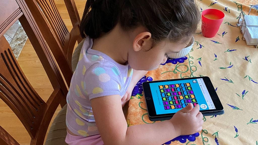 Child sitting at a table and playing an online game on a tablet.