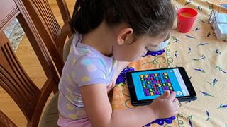 Child sitting at a table and playing an online game on a tablet.
