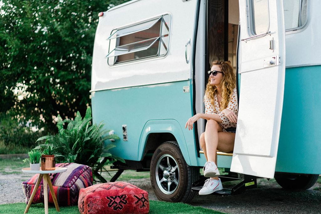 Woman sitting on the step and doorway of a teal coloured camper