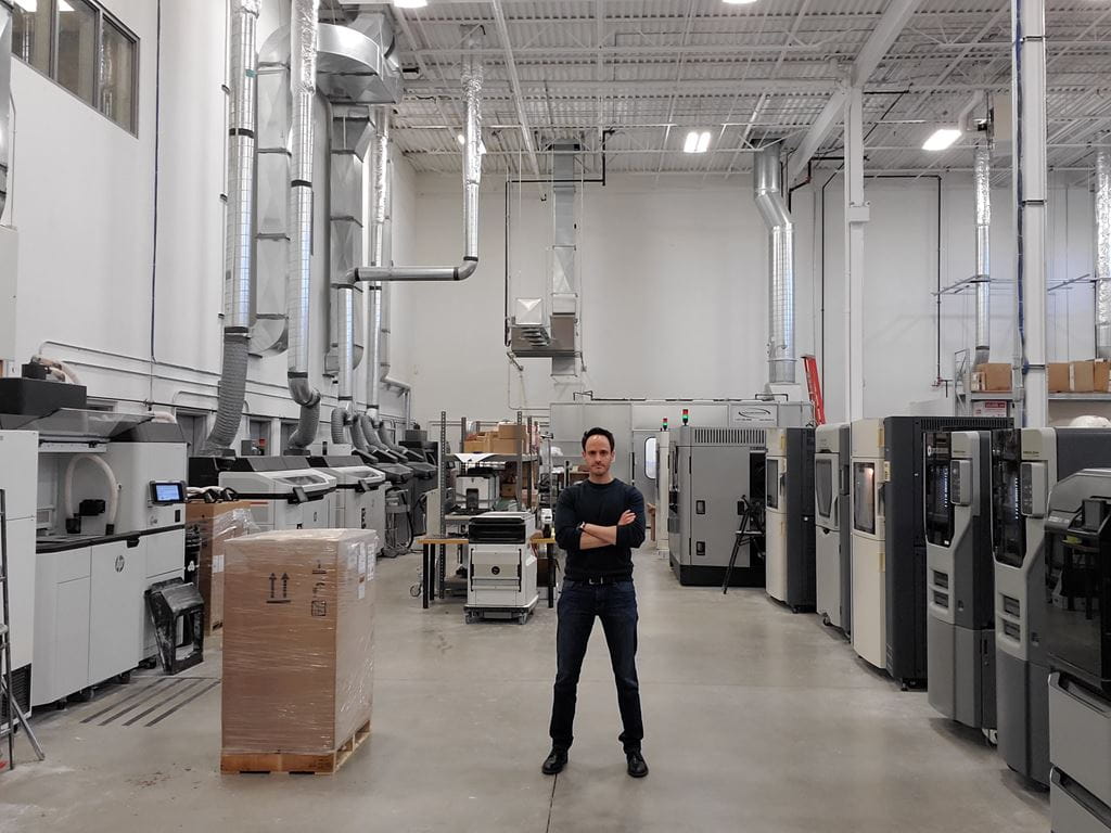 Eyal Geiger standing in front of additive manufacturing equipment.