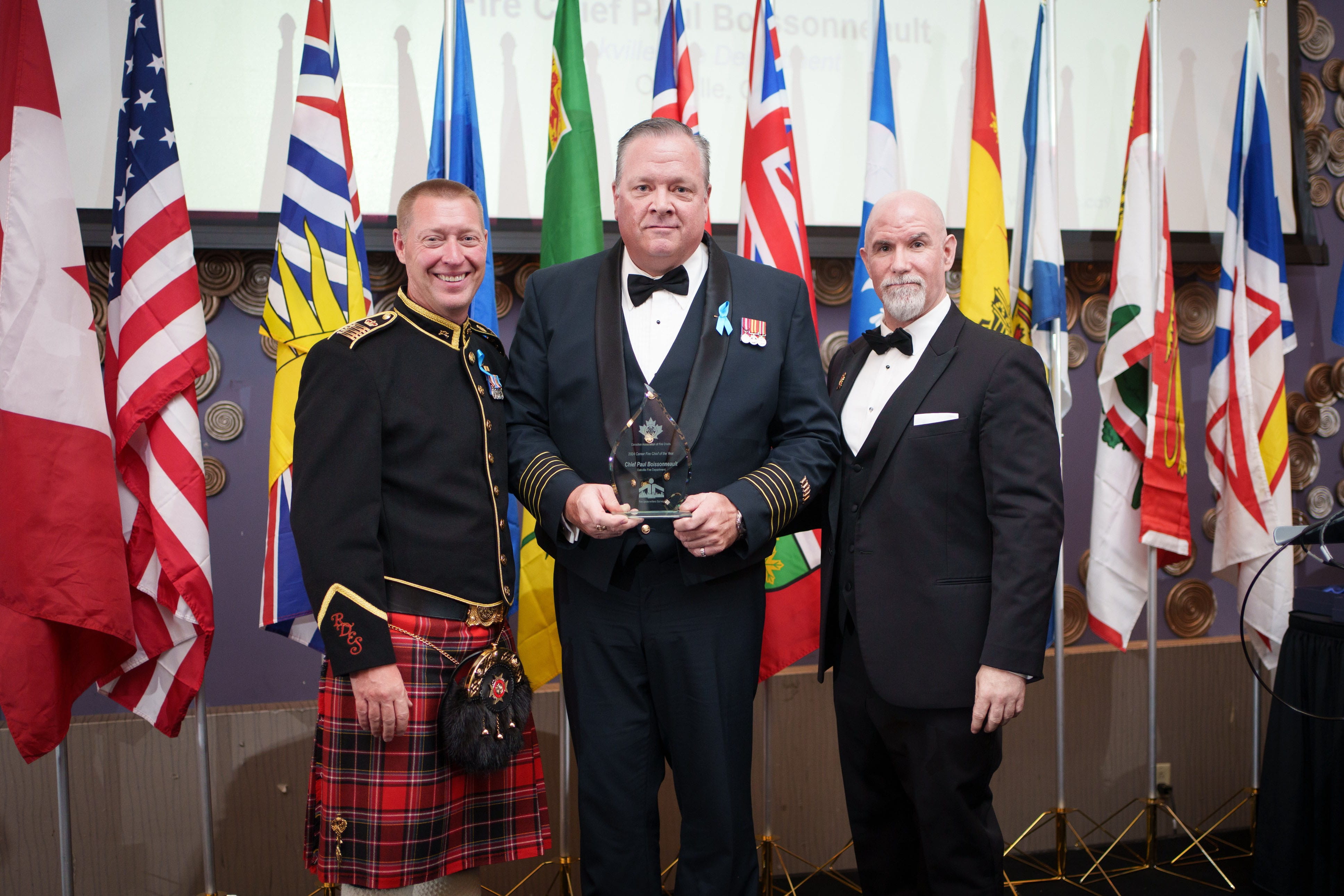 Oakville Fire Chief Paul Boissonneault stands between Canadian Association of Fire Chiefs president Ken McMullen and Fire Underwriters Survey vice-president Michael Currie, holding his 2024 Career Fire Chief of the Year Award.