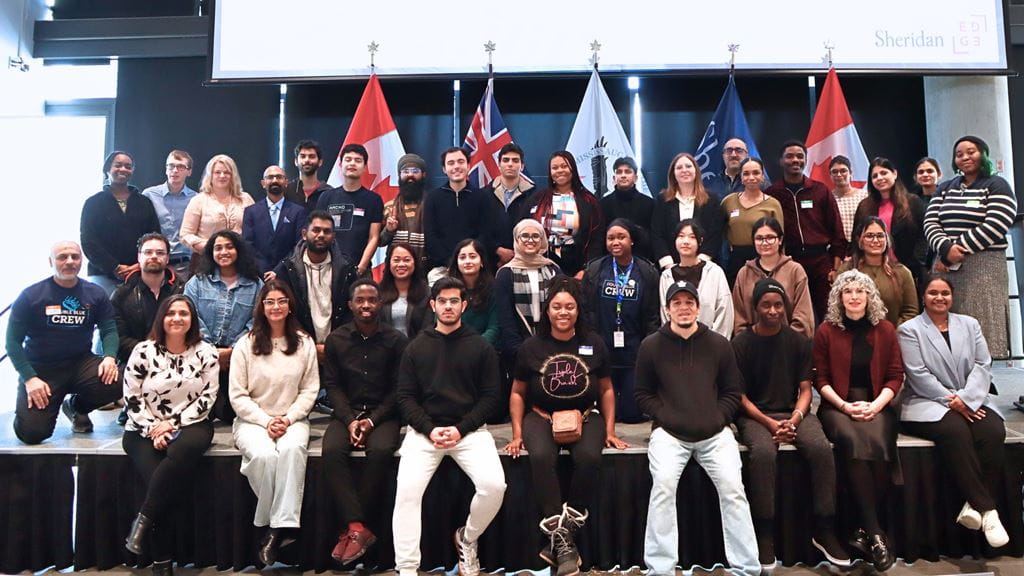 A group photo of Thrive participants on a stage with various flags in the background