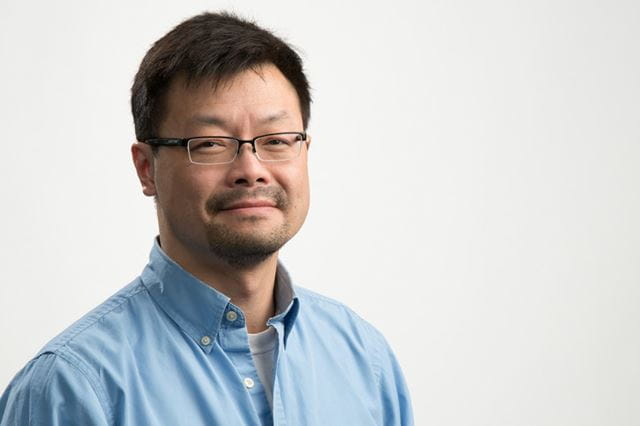 Headshot of Sheridan professor Wayland Chau, who is wearing a blue button-up shirt
