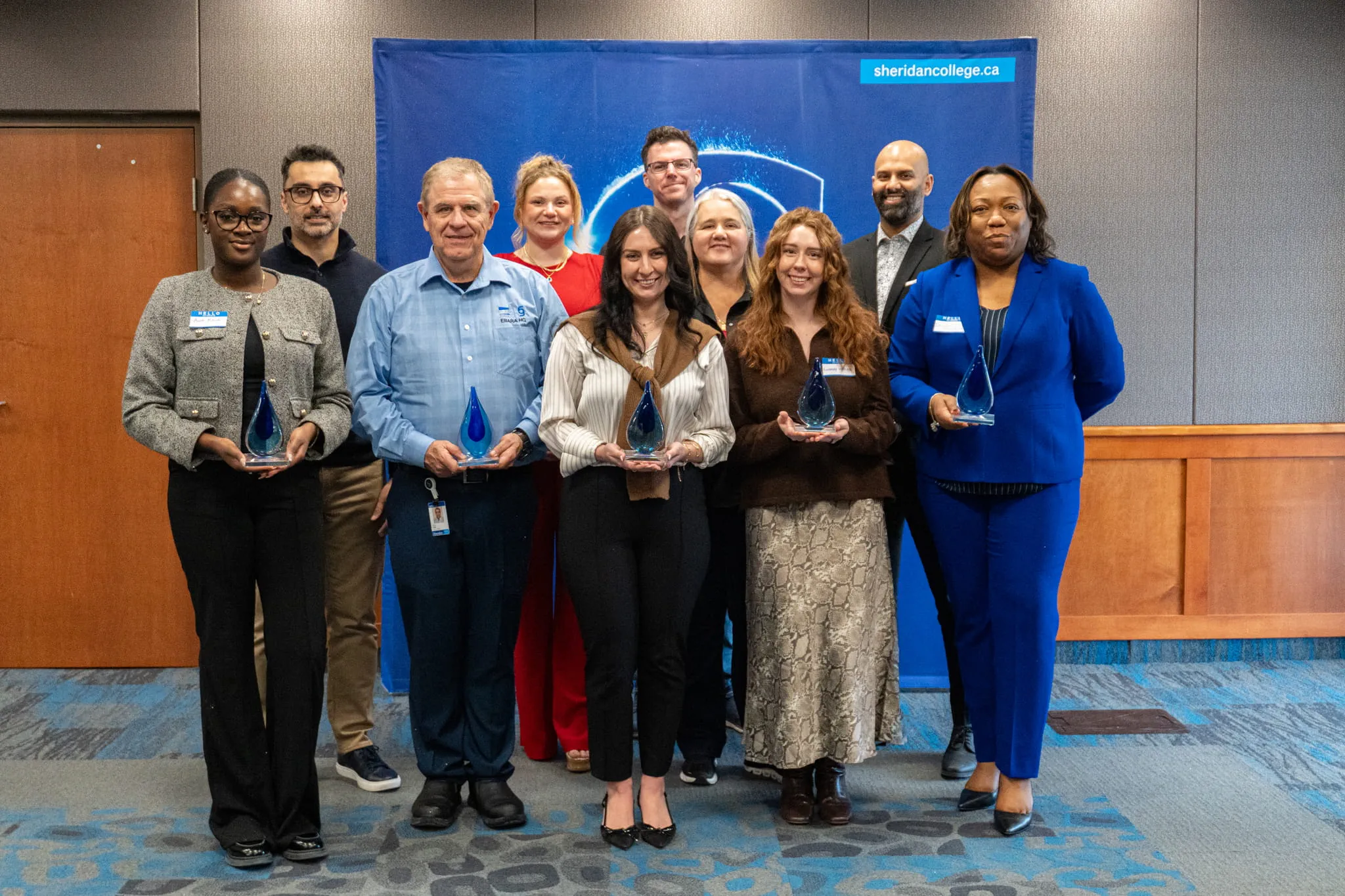 2025 Employer of the Year award recipients hold blue glass figures as they pose together for a group photo