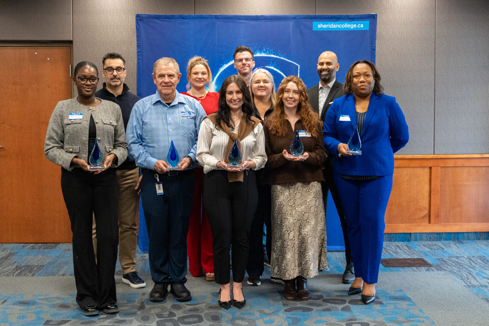 2025 Employer of the Year award recipients hold blue glass figures as they pose together for a group photo
