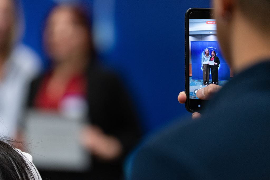 A close-up of a person using their smartphone to take a photo of a loved one receiving a Sheridan work-integrated learning student of the year award