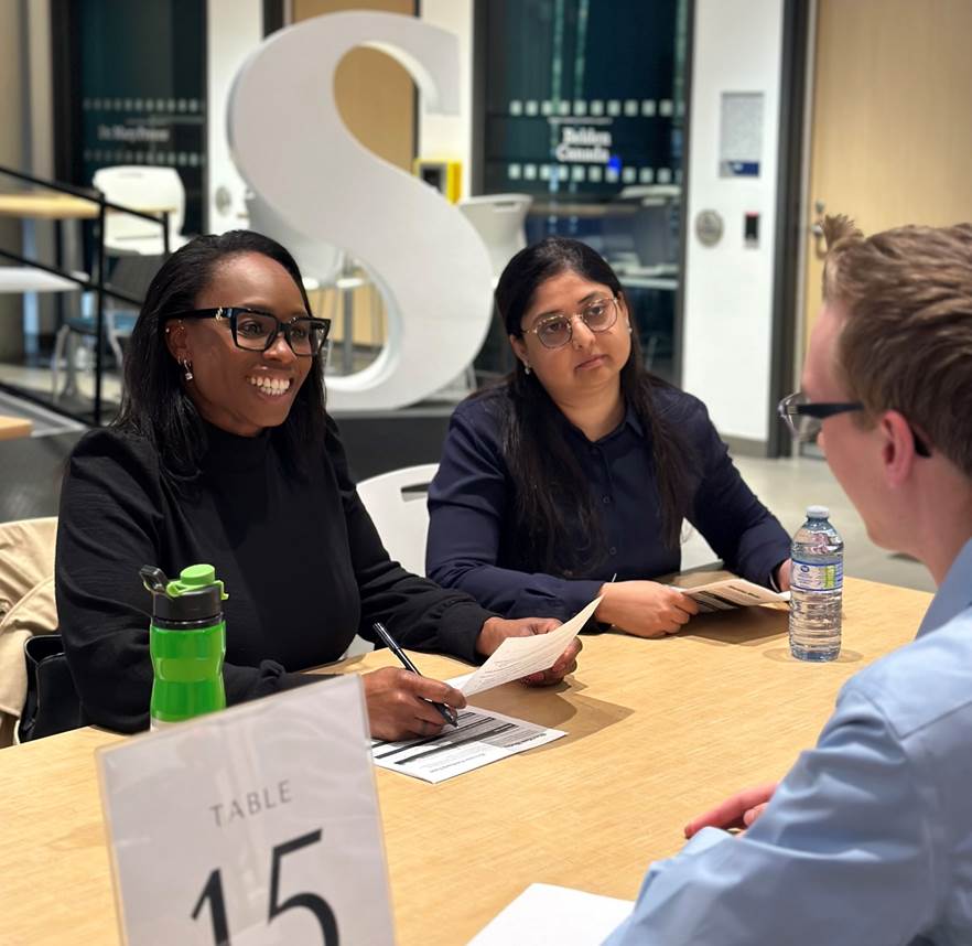 Two people sit across the table from a job applicant during a mock interview session