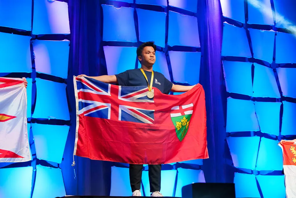 Thinh Luu holds Ontario flag on stage after receiving gold medal at Skills Canada Closing Ceremony