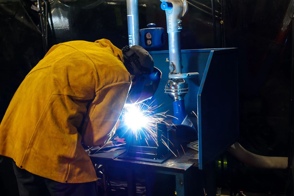 A person in a yellow safety jacket and helmet welding two pieces of metal