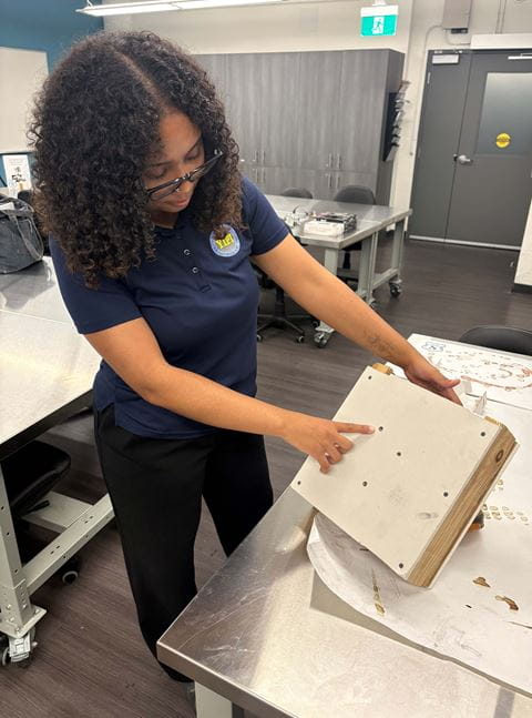 Brianna Hodgson-Douglas shows a piece of board with bullet holes.