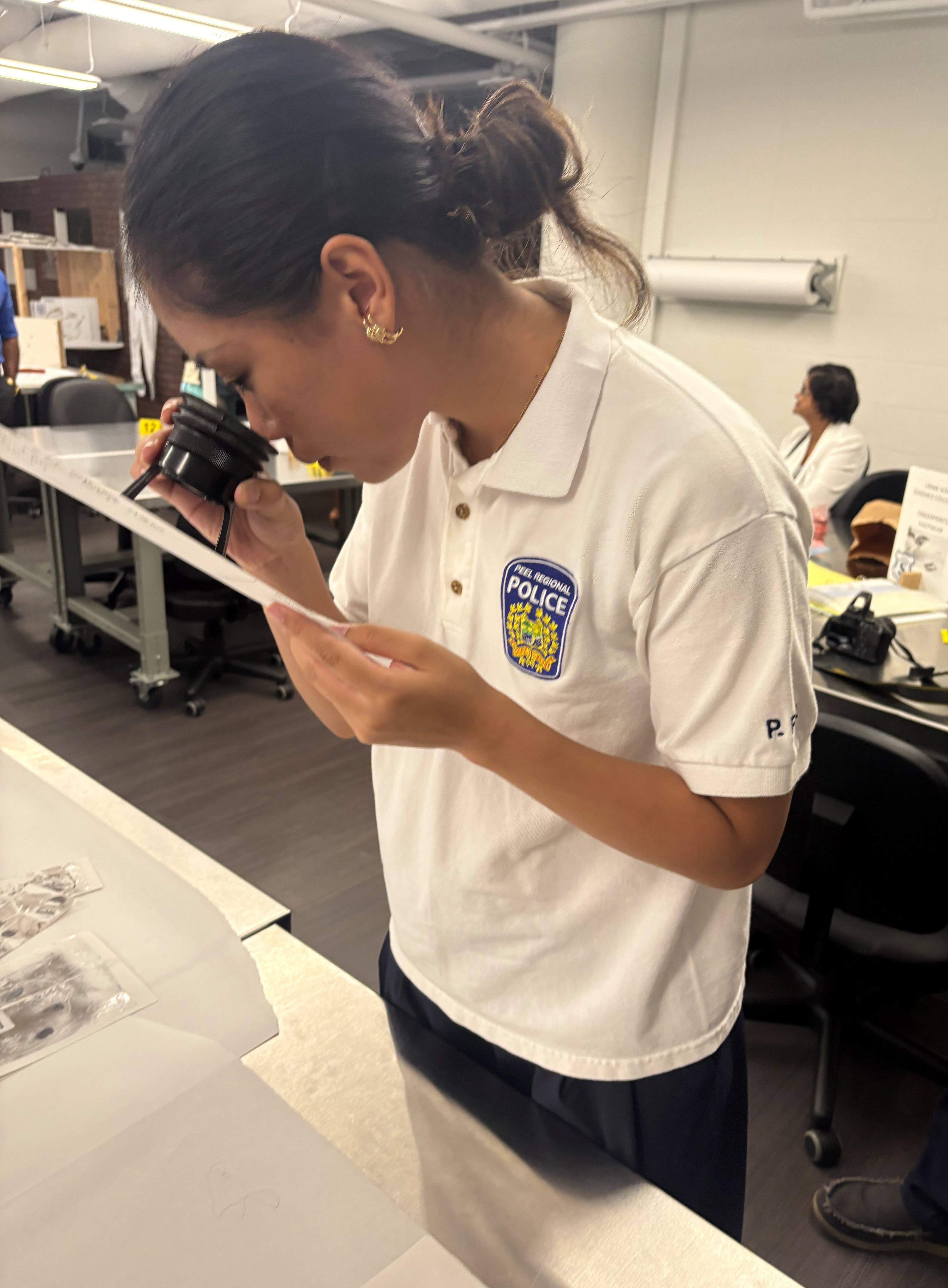 Student Sarah Chen uses a magnifying glass to look closely at a fingerprint on a paper.
