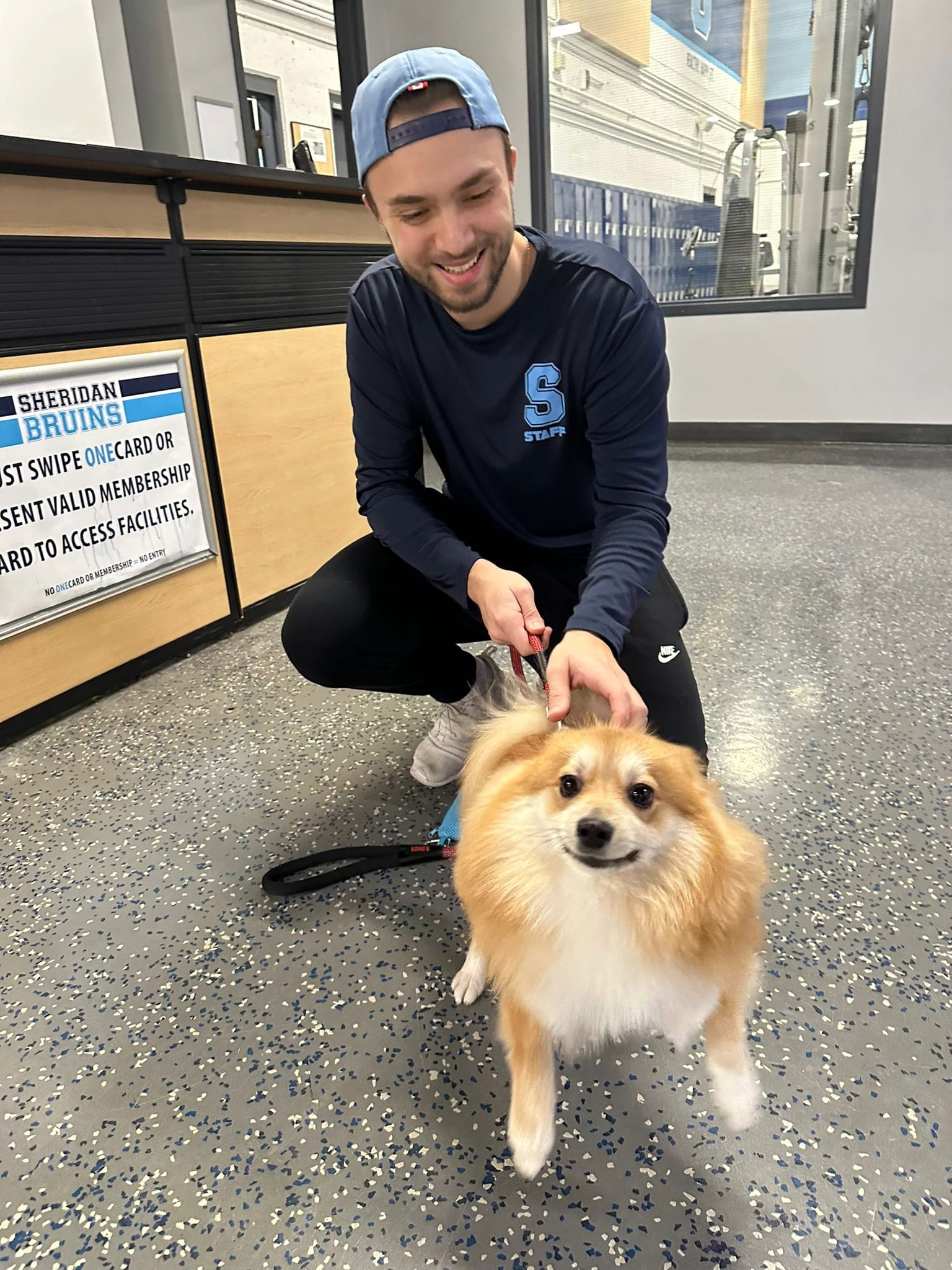 Alberto De Avila holds a dog on a leash next to the reception area at the Sheridan gym