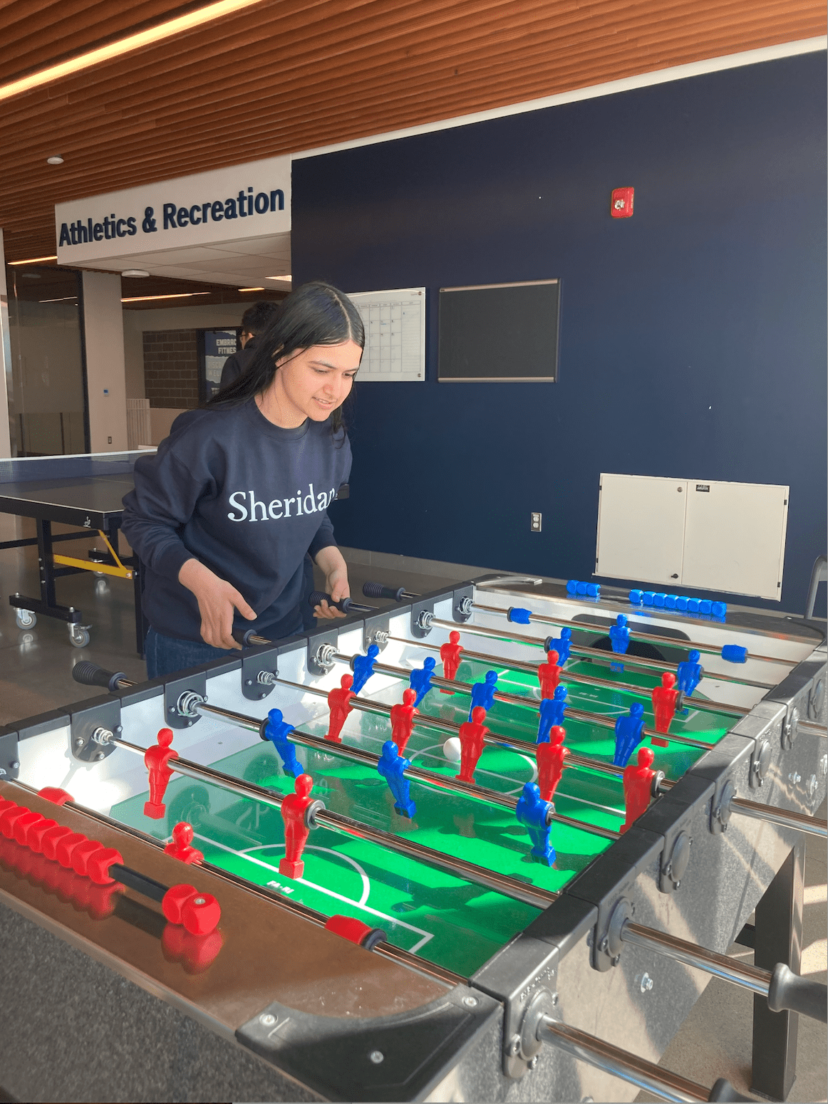 Mannat plays table soccer inside the athletics and recreation space at Hazel McCallion Campus