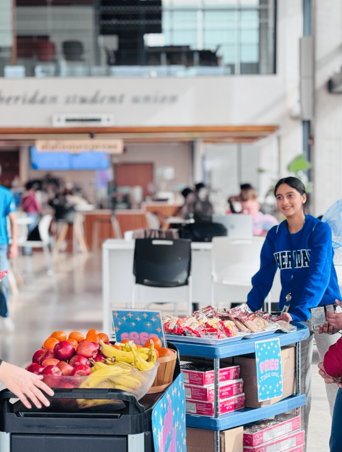 Tishika Soni stands next to bins of free food inside the Sheridan Student Union space