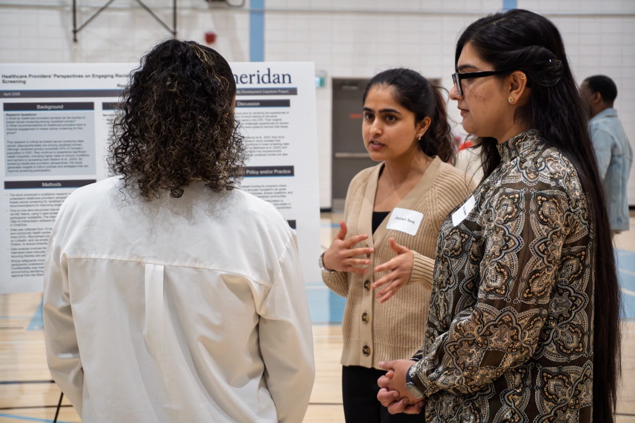 Sheridan students Jaspreet Kaur and Harleen Harleen explain their project to a symposium attendee