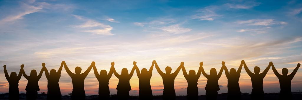 Silhouettes of people holding hands with their arms raised in the air and a sunset in the background
