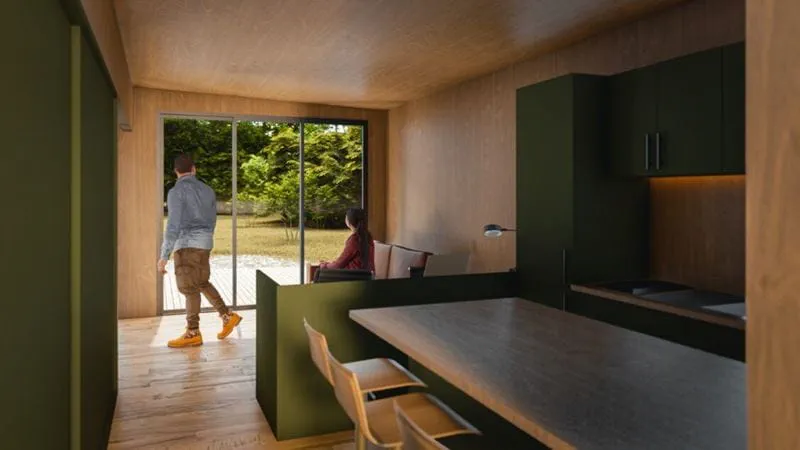 A rendering of a tiny home design in which a kitchen flows into a seating area where two people look out a sliding door into the back yard.