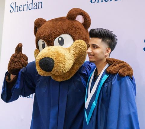 Mascot Bruno the bear poses with a graduating student.