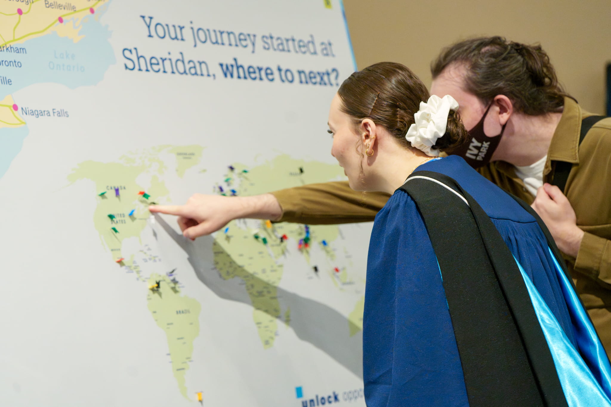Two people look at and point to a large map of the world with pins placed in it.