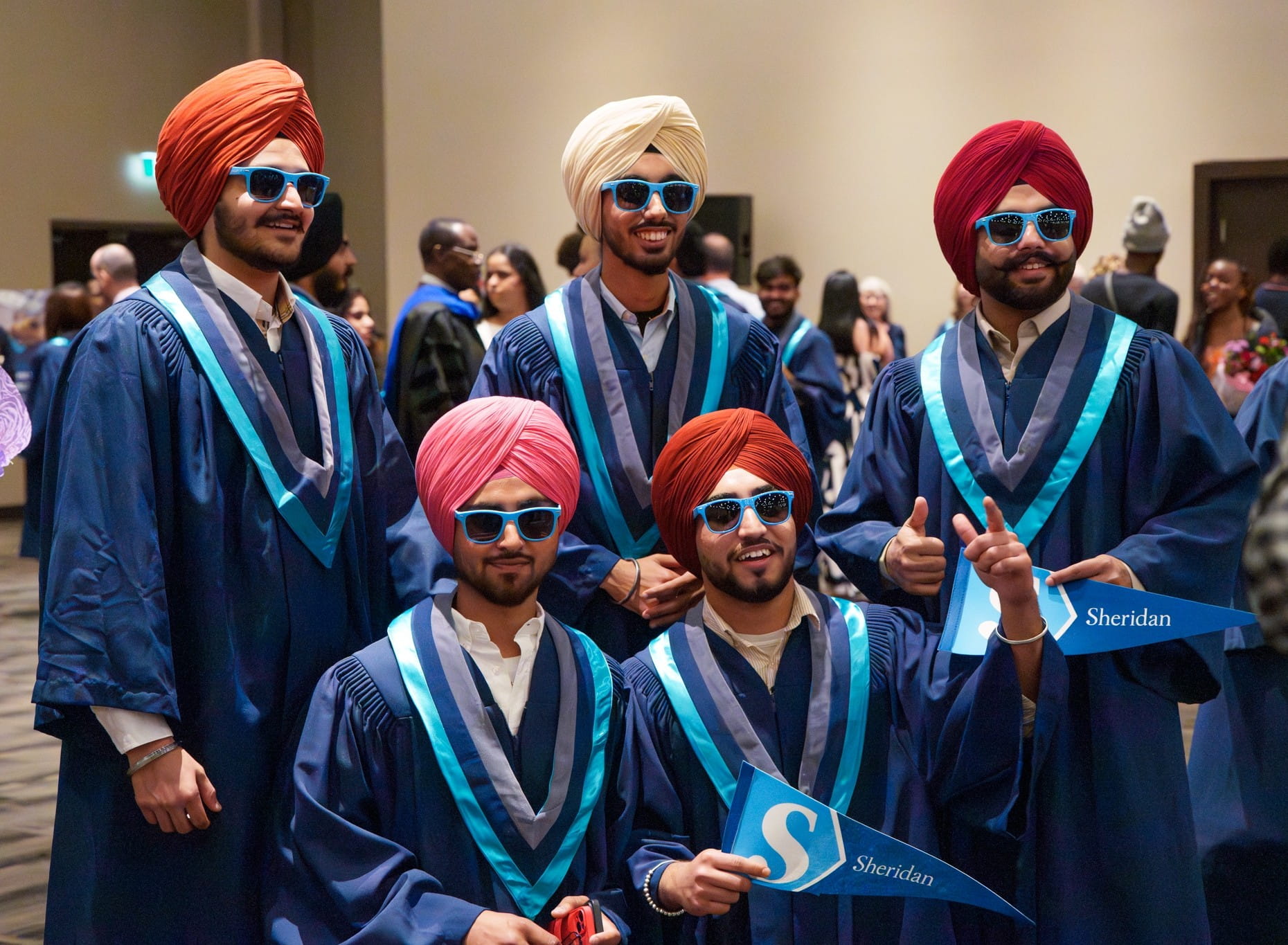 A group of graduating students, wearing robes, turbans and sunglasses, smiles at the camera.