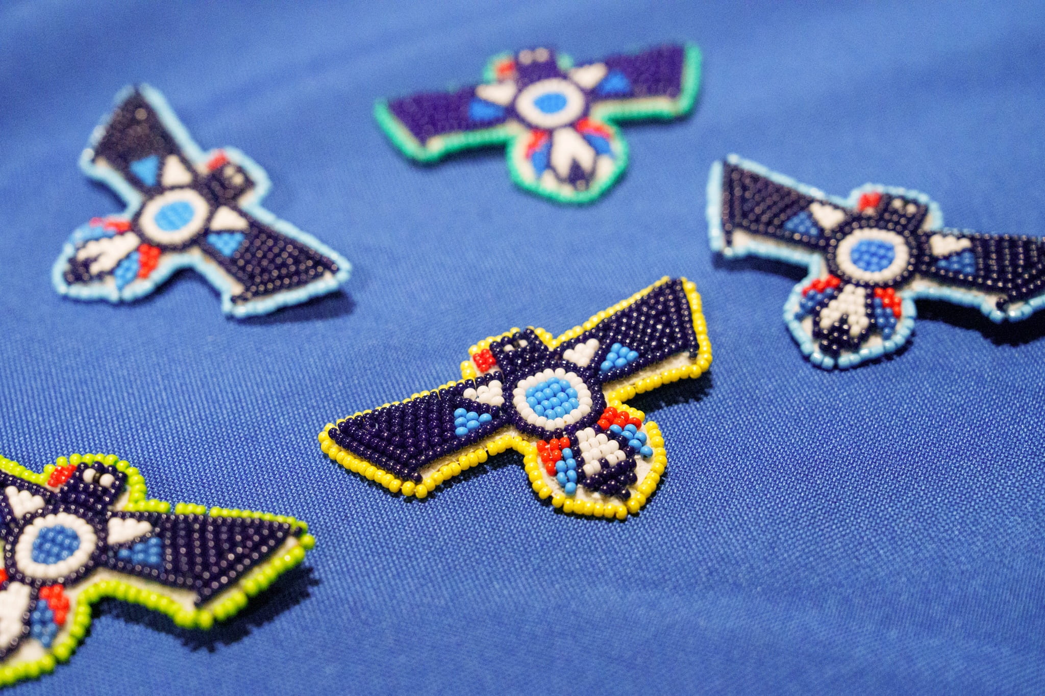 Five colourfully beaded thunderbird pins sit on a blue background.