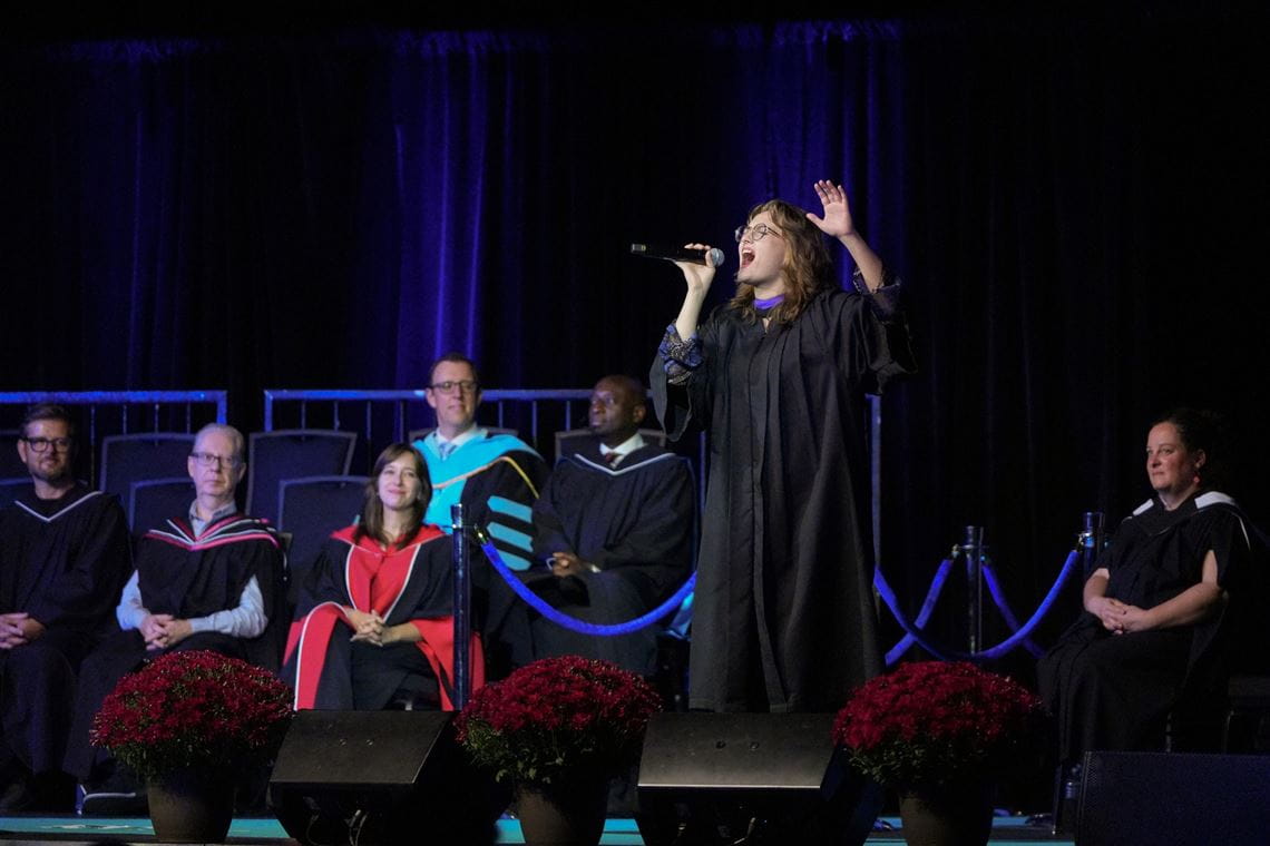 Singer Annika Tupper performs a song on stage, while members of the platform party look on.
