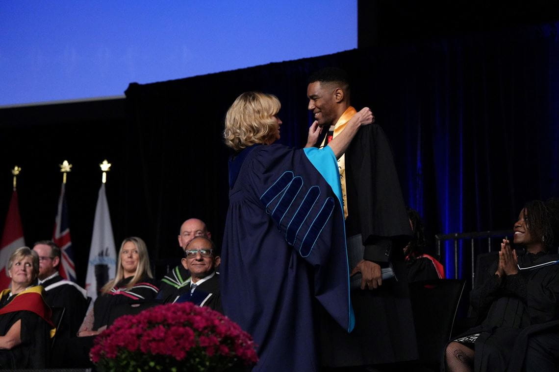 President Janet Morrison adjusts the stole of valedictorian Jason-Tyler Edwards on stage before his speech.