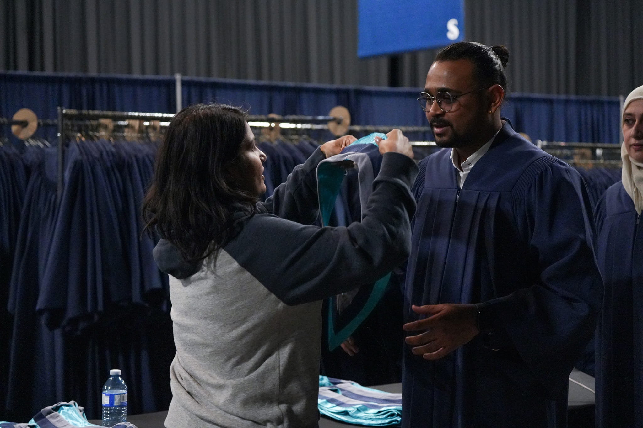 A Sheridan ambassador places a stole over a student who is wearing a blue convocation robe.
