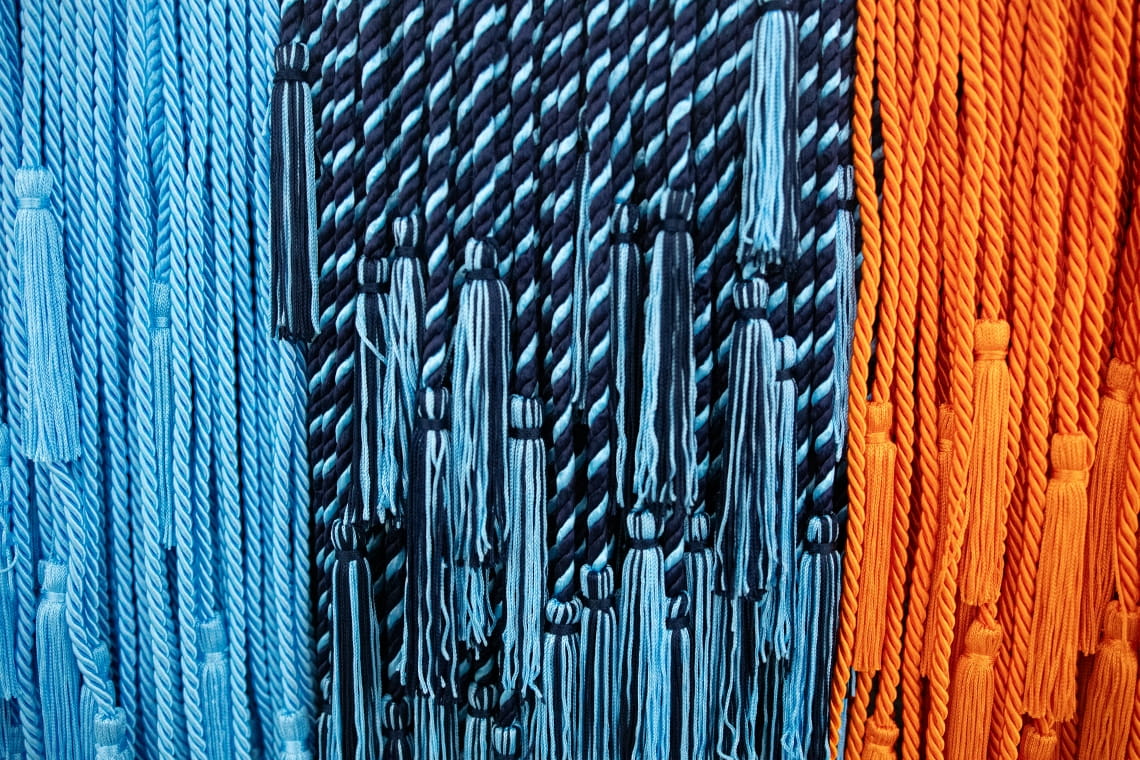 Light blue, double blue and orange cords with tassels lie on a table.