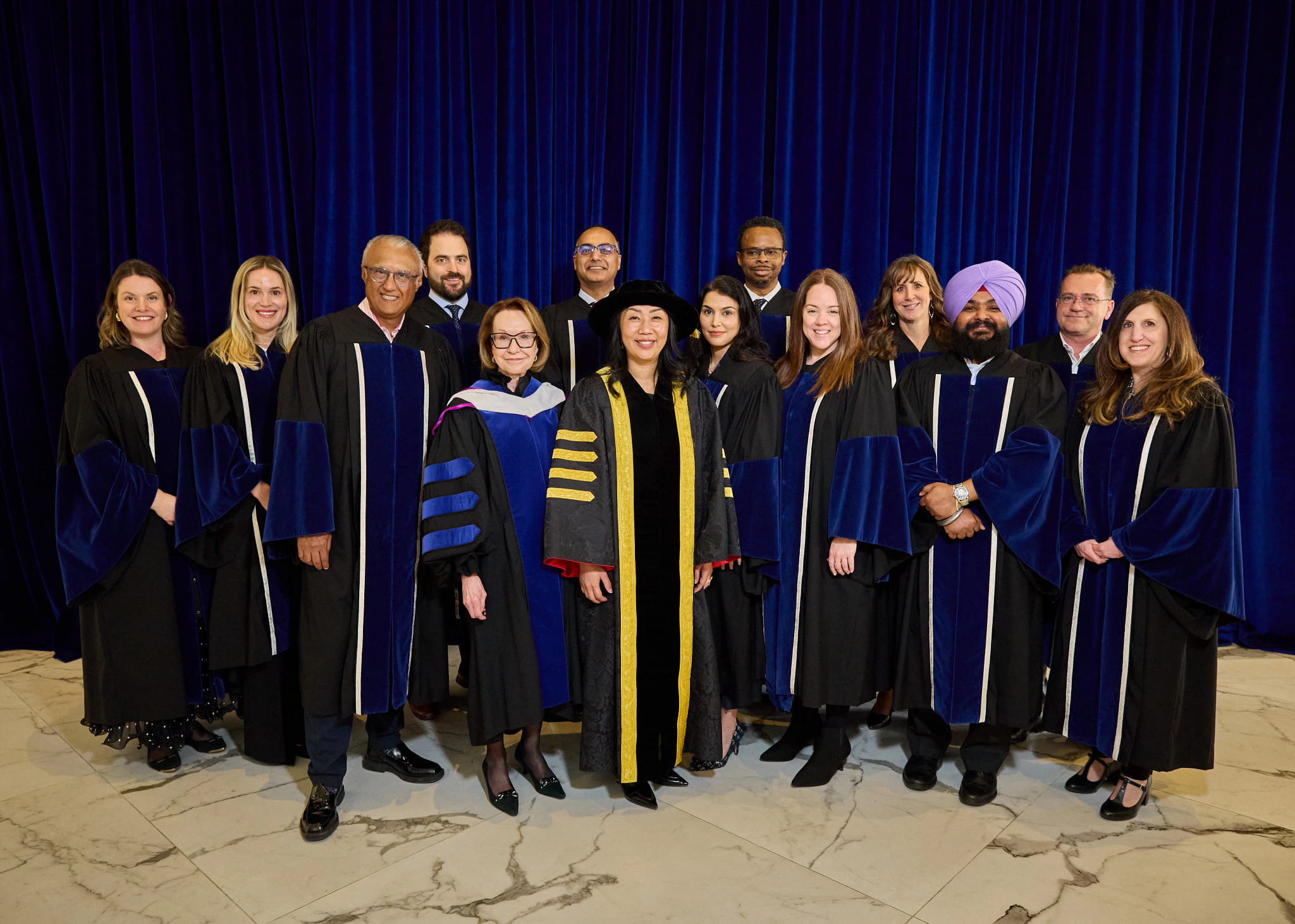 Fourteen members of the Board of Governors wearing academic robes stand in a group.