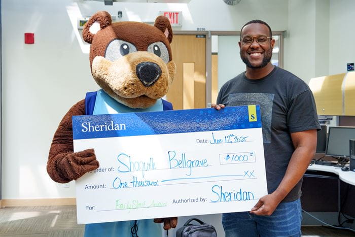Bruno the bear mascot and student Shaquille hold a large cheque for $1,000.