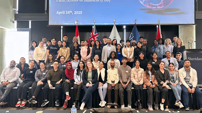 A large group of people in four rows poses for the camera. They stand in front of five flags.