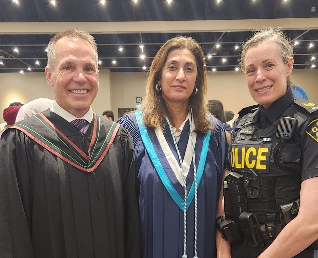 Nazia wearing a robe at convocation with two police officers