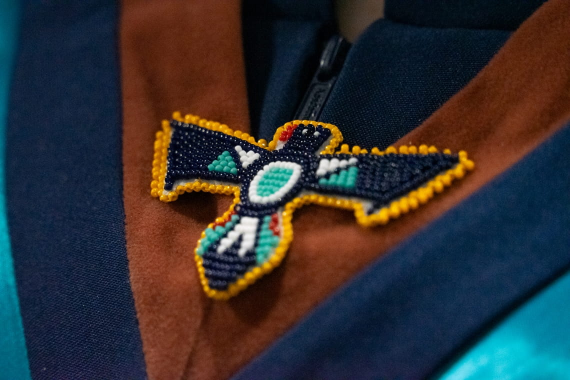 A close-up photo of a hand-beaded thunderbird pin which is pinned to the sash of a grad robe.
